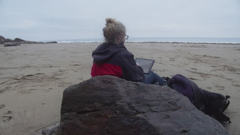 a woman sits on a rock draws on a tablet the beautiful sea view in rinsey head and cove, cornwall, england, united kingdom