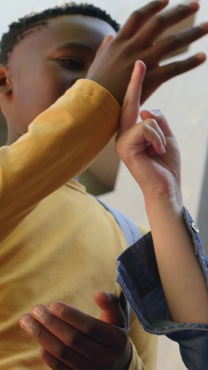 Vertical video: Fidgeting boy in mustard looking up as denim girl entering at school with backpacks