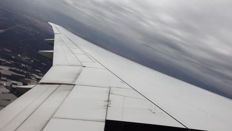 vista del ala del avión volando sobre la ciudad con techos y girando para aterrizar