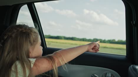 Caucasian-girl-of-8-years-looking-out-of-the-car-window-and-pointing-while-car-trip.