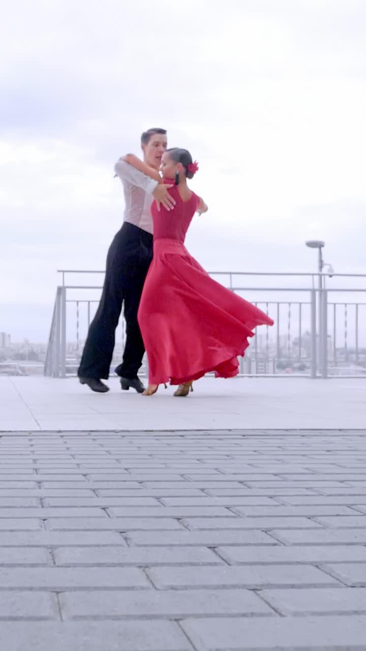 Couple dancing passionately in vibrant red attire on a modern outdoor dance floor with city view