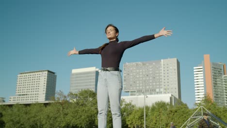 権限を与えられた若い魅力的なラテン女性が腕を開き、晴れた日にバルセロナ市の広角ショットで精神的なレベルで太陽を抱きしめる