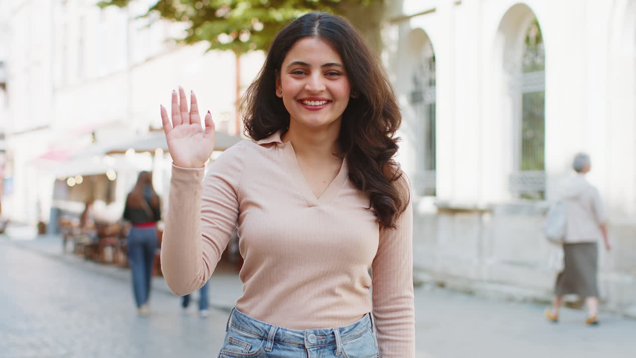 mujer india sonriendo amistosamente a la cámara agitando las manos hola hola saludo o adiós en la calle de la ciudad