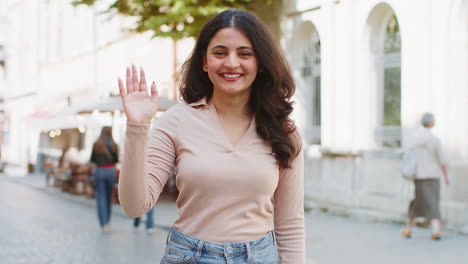 indian woman smiling friendly at camera waving hands hello hi greeting or goodbye in city street