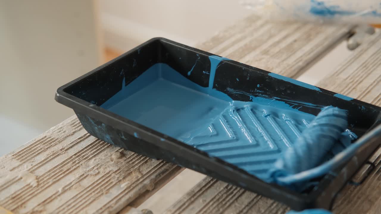 Mergulhando o rolo de pintura em tinta azul na bandeja de plástico