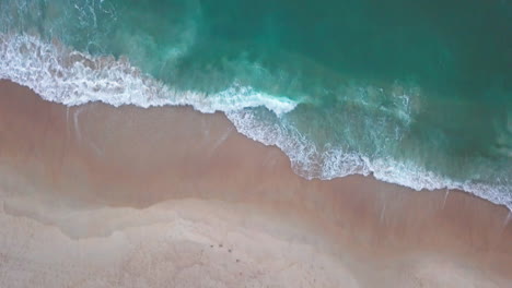 top down aerial shot of people on beach and waves crashing ashore in atlantic ocean