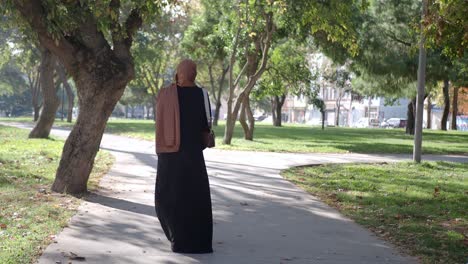 woman in hijab and abaya walking through a park