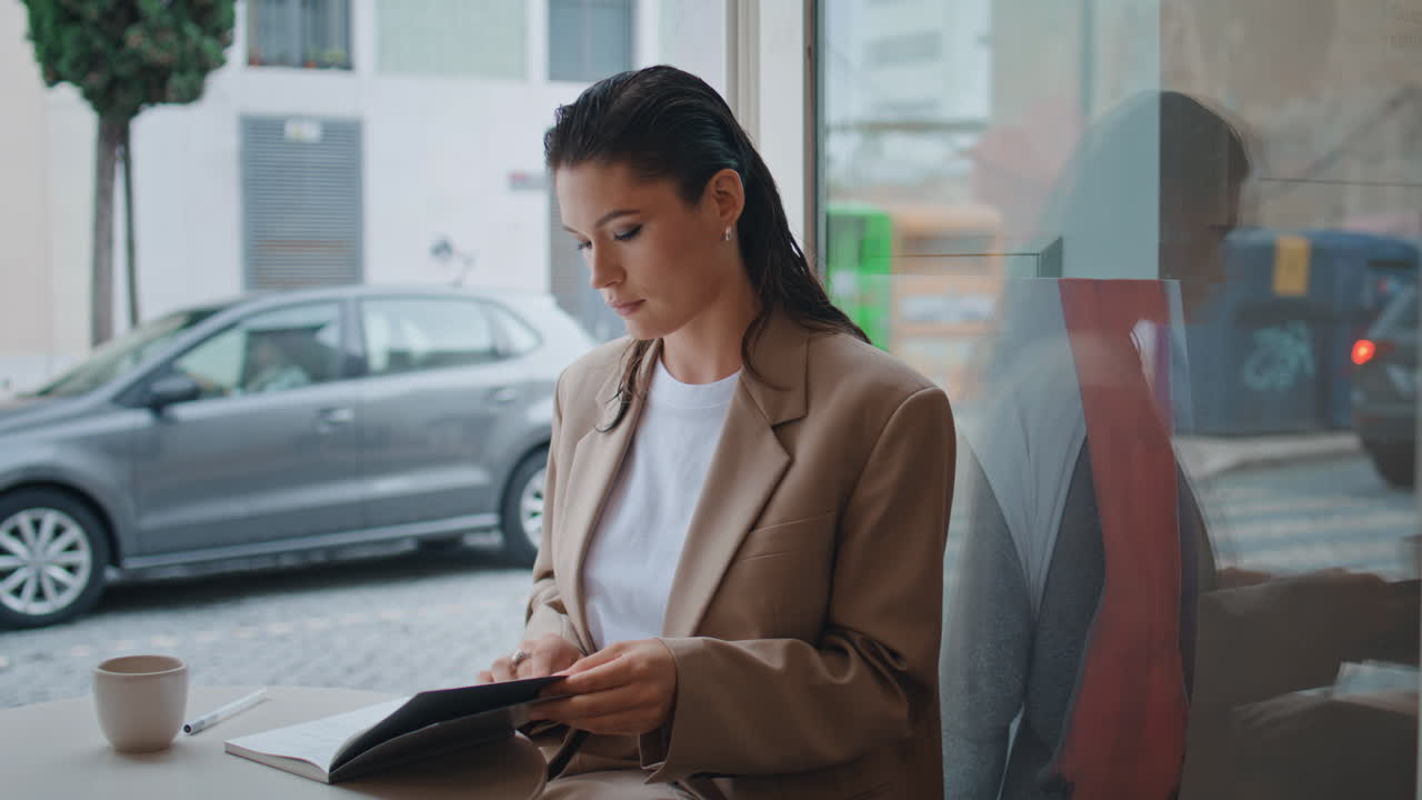 una estudiante que busca un libro de copias sentada en una acogedora ventana de la cafetería sola en primer plano.