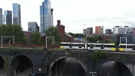vuelo aéreo de drones volando junto a un tranvía en un puente en el centro de la ciudad de manchester con vistas a los rascacielos de las torres elizabeth en el fondo