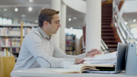 Focused-man-sitting-at-desk-and-writing-in-library