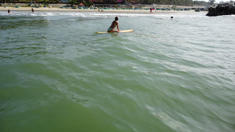 Young-caucasian-athletic-female-surfer-waiting-for-a-perfect-waves-while-surf-on-yellow-board-in-ocean-tropical-beach-seascape