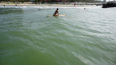 joven surfista atlética caucásica esperando olas perfectas mientras navega en una tabla amarilla en el paisaje marino de la playa tropical oceánica