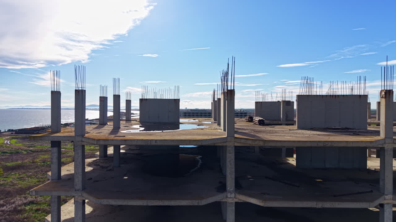 Abandoned construction site by the water under a clear blue sky with concrete pillars reaching upward toward the clouds