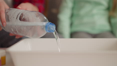 woman pours water into tray with little girl sitting on sofa