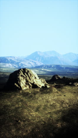 a serene landscape with a single large rock in the foreground and mountains in the distance.