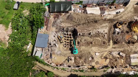aerial view of a large construction site with heavy machinery, including excavators and a crane, showing ongoing earthworks and foundation development in muddy conditions