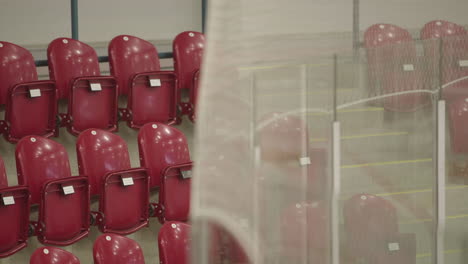 rack focus from netting above glass in ice rink to empty red folded seats. establisher shot for sporting event.