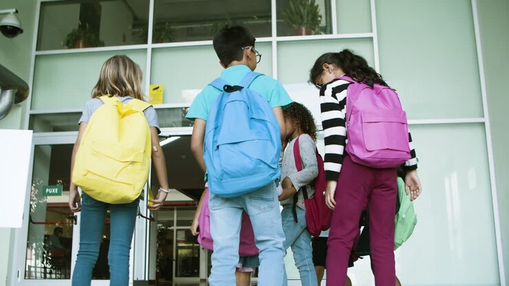 Grupo de niños de diferentes edades subiendo escaleras hacia la escuela