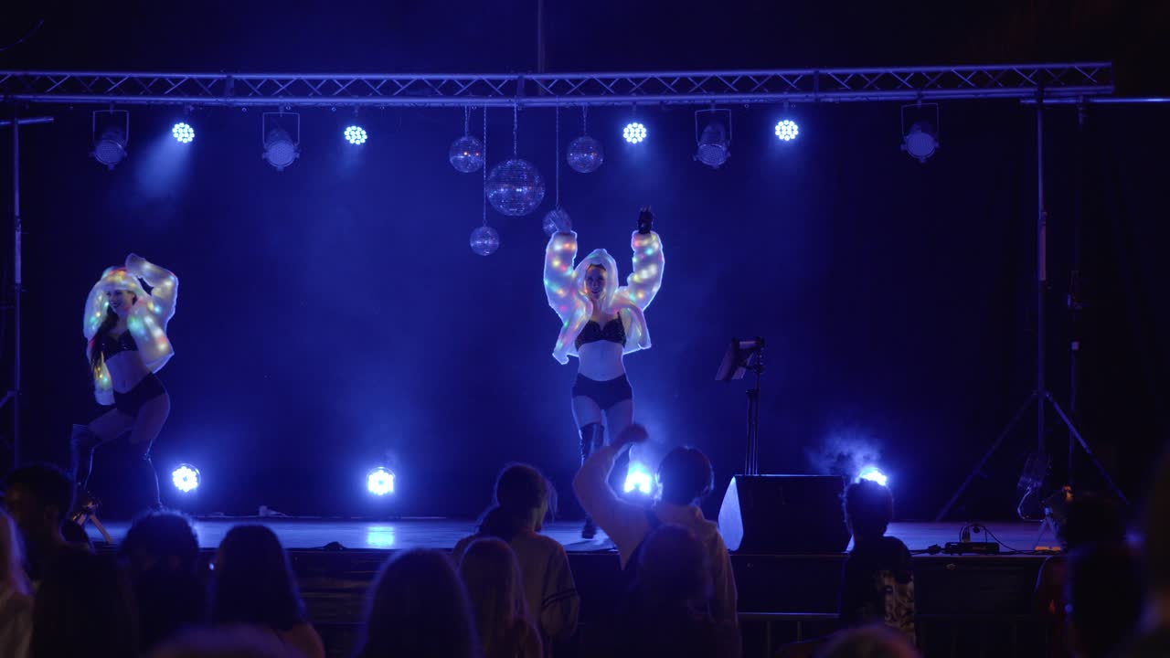 Slow establishing shot of dancers performing on stage with led outfits