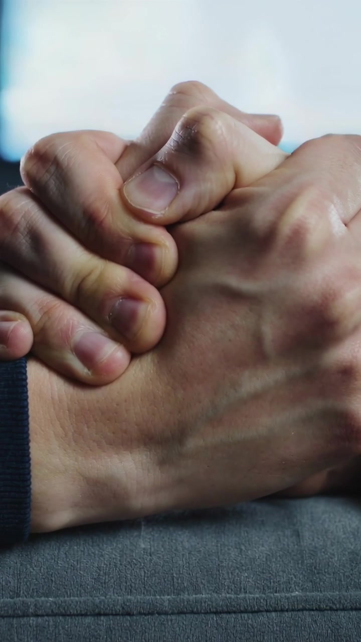 Vertical video: Clasping hands tightening on grey sofa after shift with dark sleeve and blue glow