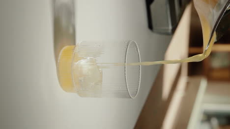 Vertical-Video-pouring-fresh-pressed-orange-juice-into-drinking-glass-in-the-kitchen-slow-motion-close-up