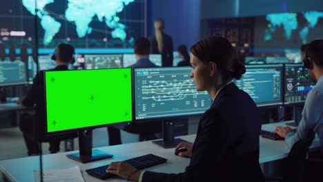 una mujer científica de datos confiada trabaja en una computadora personal con una maqueta de pantalla verde en una gran sala de control y monitoreo de infraestructura. una mujer ingeniera usa la computadora en una habitación de oficina con colegas.