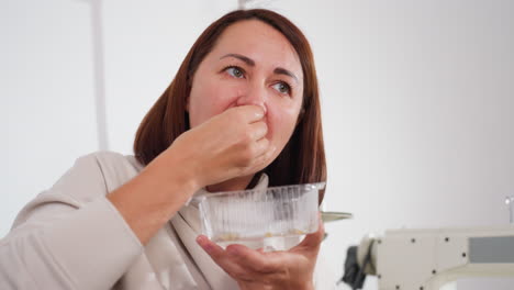 elegant woman enjoying bite of chicken while holding clear disposable plate, casual indoor setting with sewing machine in background, content expression on her face showing satisfaction with meal