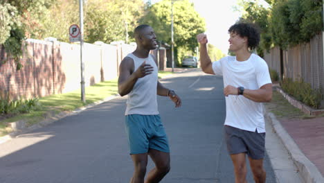 two multiracial male friends greeting each other with handshake and hug on suburban street
