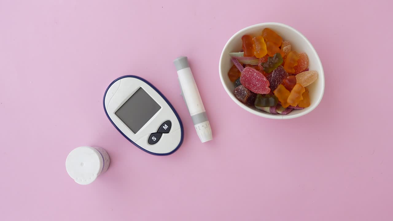 Diabetes testing kit and colorful candy on a pink background