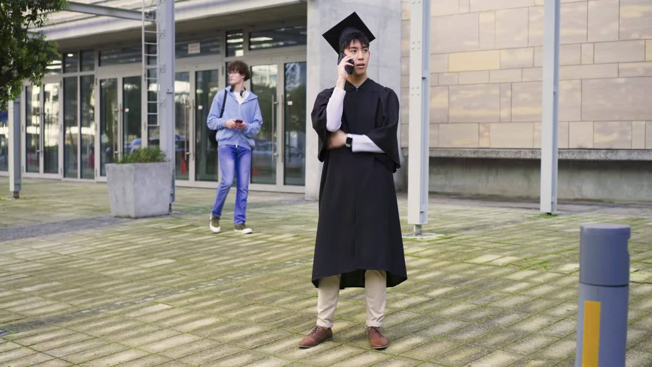 正装した卒業生が、学校の前で電話を受けている。