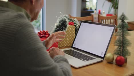 Caucasian-senior-man-sitting-at-table-making-video-call-at-home-on-laptop-with-copy-space-on-screen