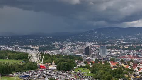 a close-up shot from a drone shows the ferris wheel and the tivoli at ekebergsletta during the norway cup 2023 with the center of oslo in the background