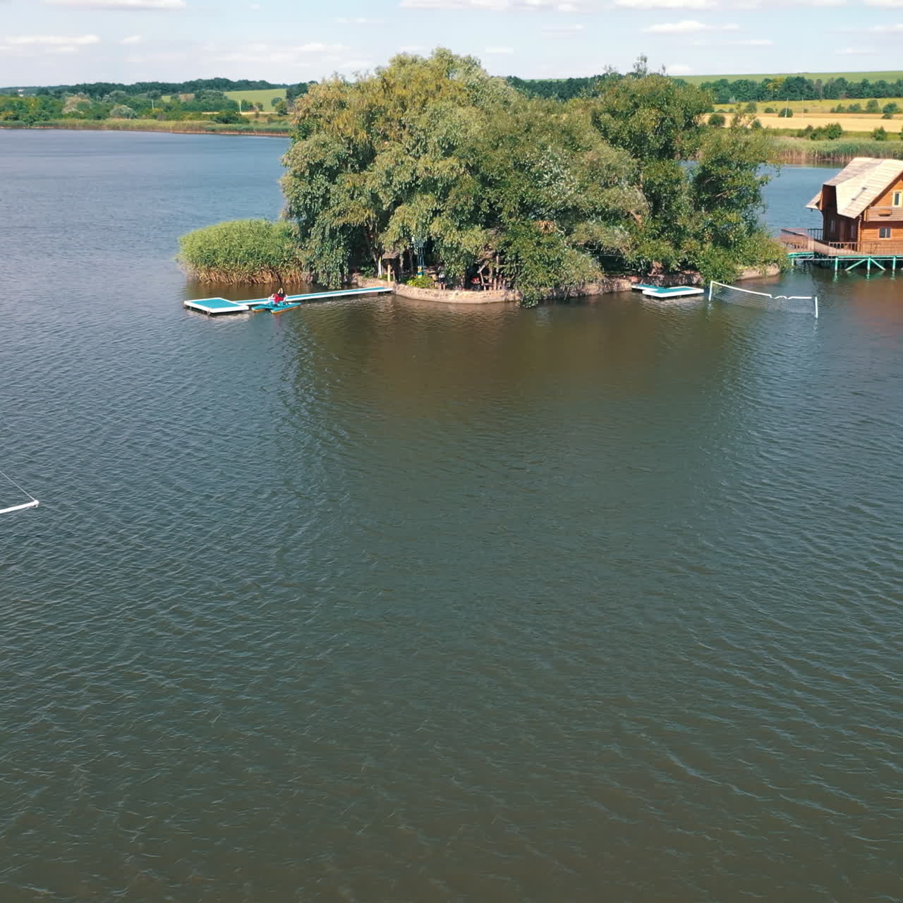 Old boat floating near the island with house in the river. Island with green trees surrounded by water on the natural background in summer. Aerial view.