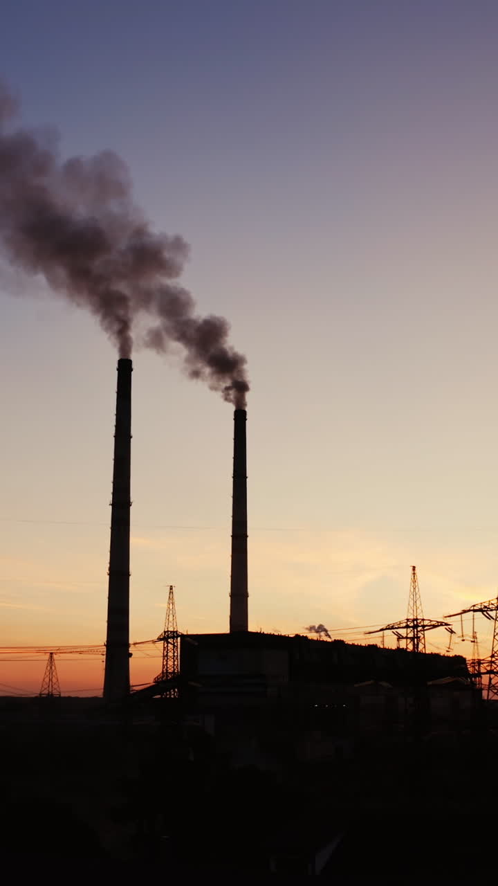 Factory tubes on the sunset background. Smoke from the pipes. Pollution concept. Video from the air. Vertical video