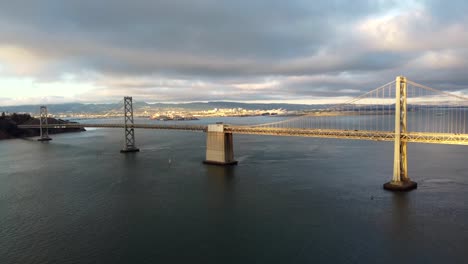 Tracking-In-Drohnenaufnahmen-Aus-Der-Luft-Von-San-Francisco-Oakland-Bay-Bridge-über-Die-SF-Bay---Autofahrt-Auf-Der-Interstate-80,-Segelboote,-Bewölkte-Cumulus-Wolken,-Ruhiges-Wasser,-Sonne,-Die-Von-Wellen-Reflektiert-Wird-4k-30fps