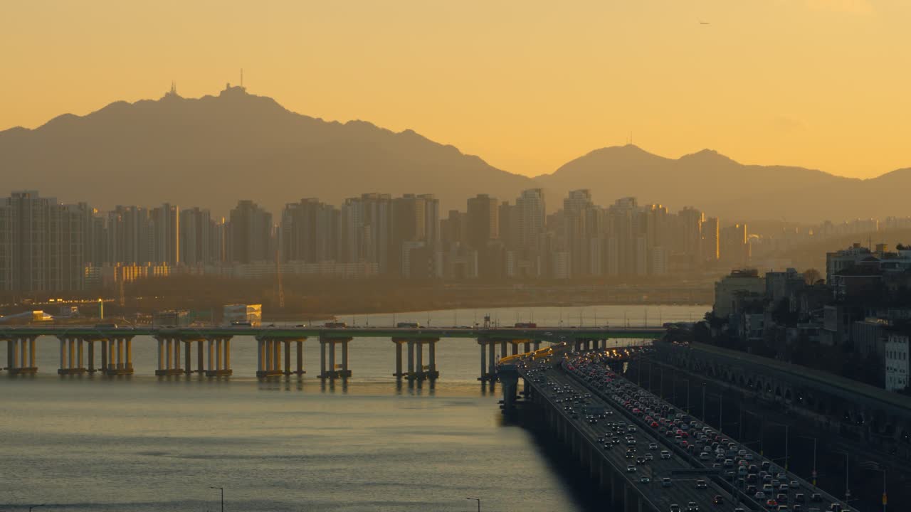 Panoramica aerea pittoresca del paesaggio urbano di Seul nella luce dorata del tramonto con traffico intenso sul ponte di Hannam e sull'autostrada Gangbyeonbuk-ro, con appartamenti di lusso e la sagoma imponente delle montagne