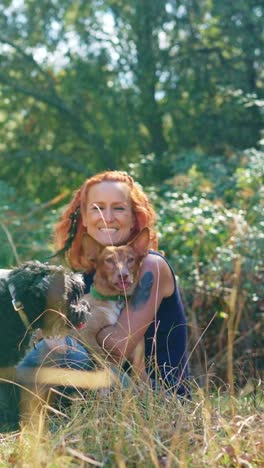 a woman affectionately hugging her two dogs in a natural outdoor setting