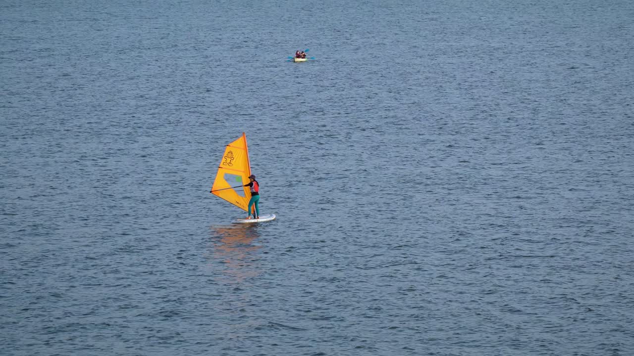 chica en forma haciendo windsurf en el río han cerca del parque ttukseom hangang en el club de surf de seúl, dos personas remando en un kayak en el fondo, corea del sur