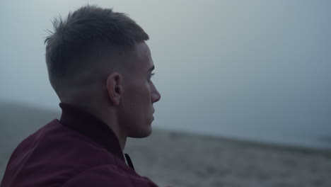 stressed guy looking ocean landscape in morning. worried man sitting on beach