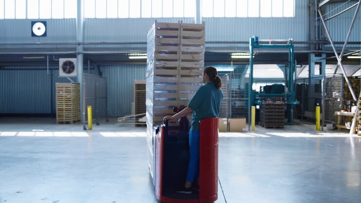 Woman warehouse worker transporting pallets driving storage machine moving boxes