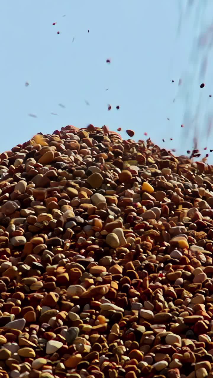 Crushed stone and gravel tumbling down a large pile as it's dropped from a conveyor belt - close-up slow-motion