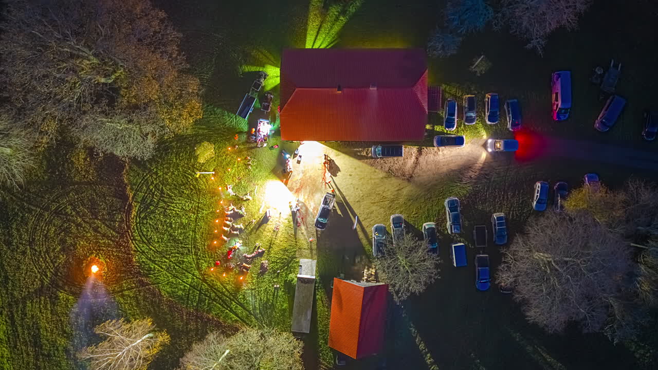 Aerial night view of a lit-up house with parked cars and trees around