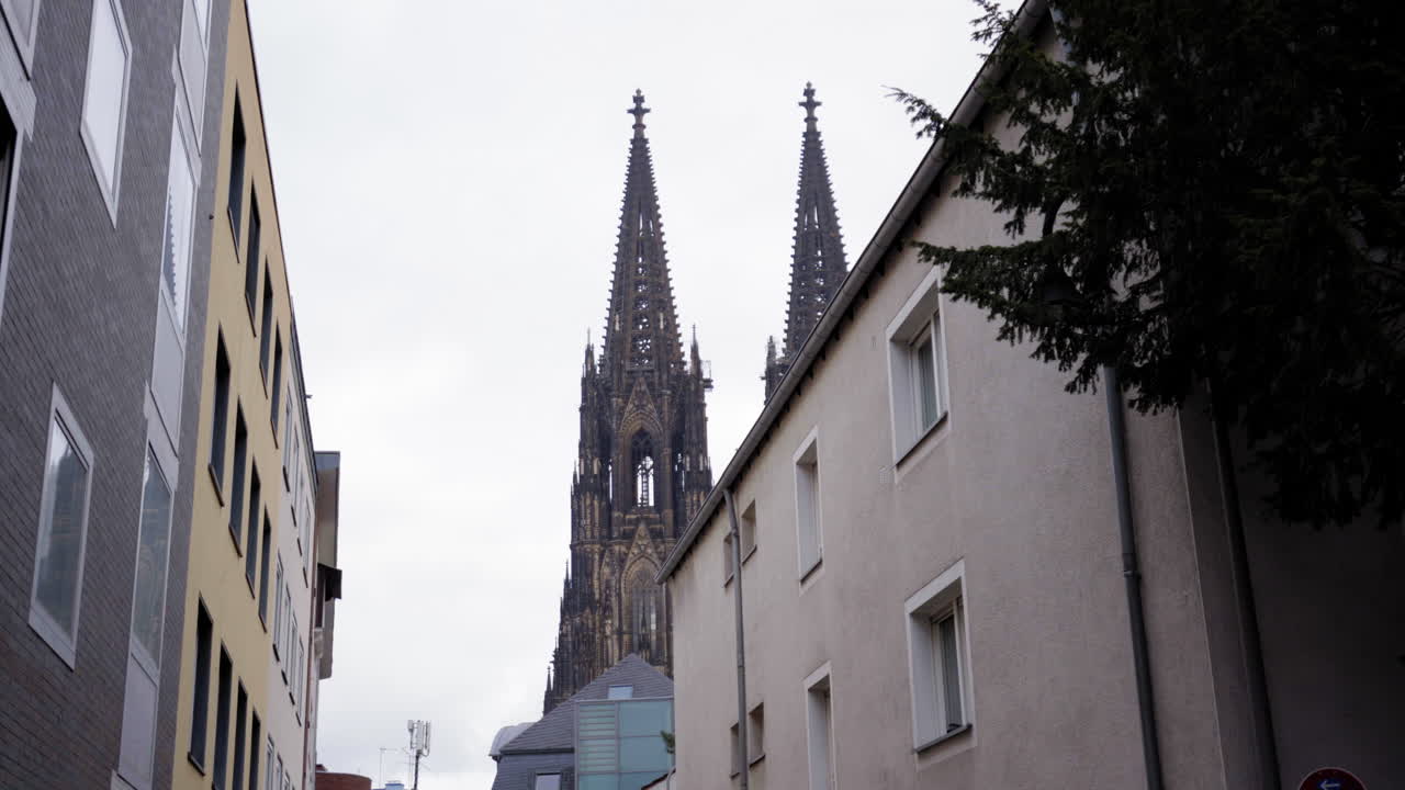 A stunning view of Cologne Cathedral's iconic twin spires framed by modern urban buildings, blending historic charm with contemporary cityscape.