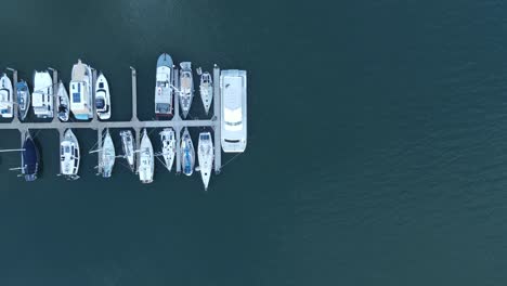 A-static-high-drone-view-looking-down-at-multiple-boats-docked-on-a-wharf-in-a-protected-harbor-located-in-the-town-of-Bargara-Bundargerg-Queensland-Australia