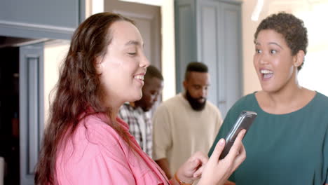 showing smartphone to friend, woman smiling and friend reacting with surprise