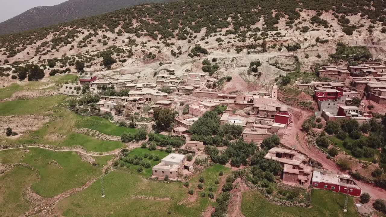 Ampia ripresa aerea che cattura uno vasto villaggio rurale situato ai piedi dell'Alto Atlante. Il filmato evidenzia l'integrazione degli insediamenti abitativi tradizionali all'interno della natura aspra.