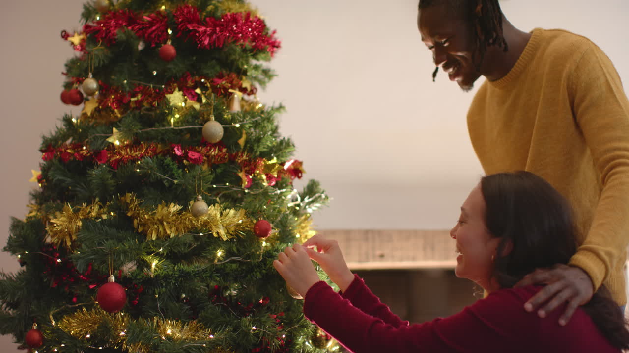 una pareja feliz decorando el árbol de navidad en casa, en cámara lenta.