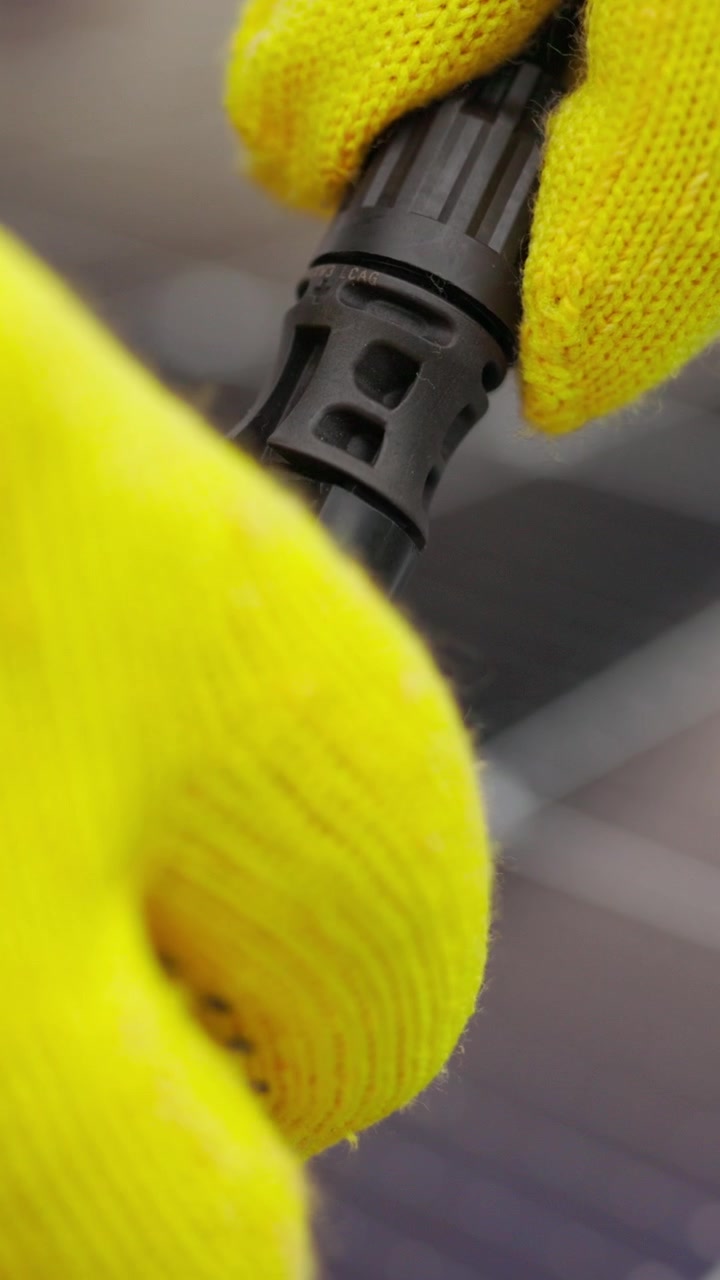 A closeup shot of a hand in a yellow glove connecting a black connector likely for a solar panel