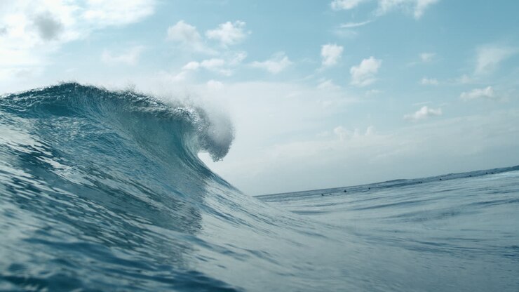 Sunlight shimmers on ocean as wave curls and crashes in open tropical sea, slow motion curl at surf break