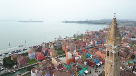 ascending aerial of the church of saint martin bishop bell tower in burano, an island province of venice in italy on a foggy day.